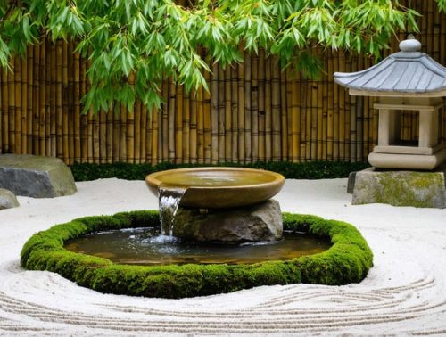 Tranquil Japanese garden scene featuring a bamboo tsukubai fountain, stone basin, moss, stones, and a traditional stone lantern amidst a backdrop of zen sand and Japanese maples.